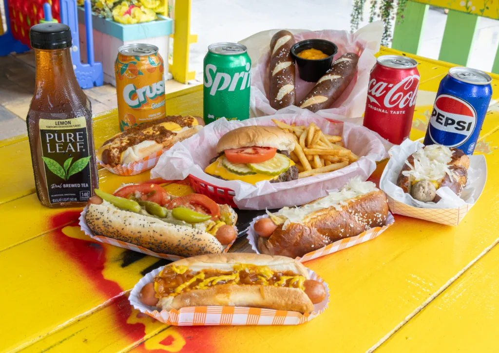 Assorted hot dogs, cheeseburger, fries, and drinks on a yellow table
